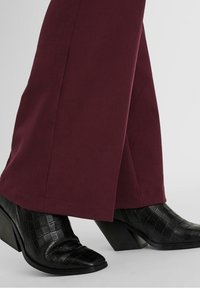 Bordeauxkleurige broek gecombineerd met zwarte, gestructureerde hoge hakken met een spitse neus en een chunky, stijlvolle hak.