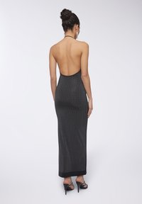 Abito maxi nero senza schienale con motivo a pois argentati. Presenta una vestibilità slim e un orlo che arriva fino alle caviglie. Abbinato a sandali neri con tacco.
