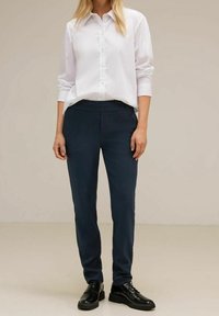 White button-up shirt with long sleeves, paired with navy tailored pants and black shoes, creating a fitted, professional appearance.