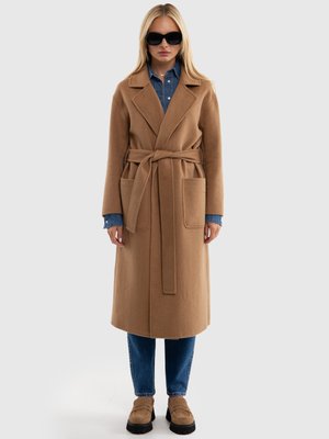 Lungo cappotto color cammello con vita aderente, colletto a revers e due tasche anteriori, abbinato a una camicia di jeans e jeans scuri.