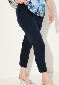 Marinblå stretchbyxor med smal passform och delad fåll, kombinerat med silverfärgade klackskor. Tyget har en slät, mjuk textur.