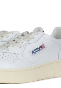 Sneakers bianchi in pelle con punta perforata, suola in gomma beige e lacci beige. Presentano il logo "AUTRY" in blu con una piccola bandiera americana.