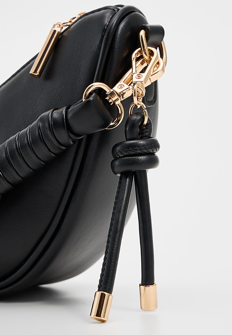 Zwarte leren handtas met een ronde vorm, voorzien van gouden hardware, een gevlochten textuur op de schouderriem en decoratieve hangaccents.