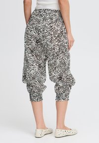 Pantaloni harem a righe in bianco e nero con cintura elastica e polsini arricciati, realizzati in tessuto leggero. Scarpe piatte e morbide visibili.