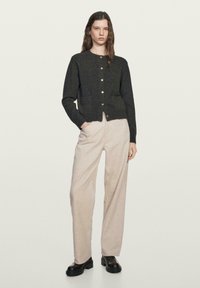 Ciemnoszary dziany kardigan z okrągłym dekoltem, zapinany na guziki z przodu, z dwoma przednimi kieszeniami, noszony z jasnobeżowymi szerokimi spodniami.