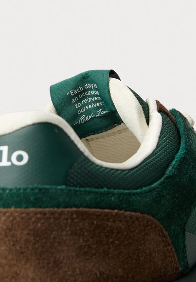 Sneaker verde și marron din material suede și plasă, având o limbă căptușită și un citat inspirațional pe eticheta din interior.