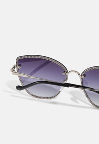 Gafas de sol angulares con lentes gradient de color púrpura, detalle en forma de cadena de plata en el marco y varillas negras. Incluye acentos de metal pulido.