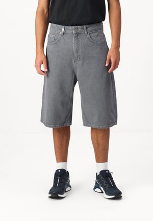 Graue Jeansshorts mit lockerem Schnitt, fünf Taschen und Knopfverschluss. Sie zeichnen sich durch eine glatte Textur und ein knielanges Design aus und werden mit schwarzen Sneakers kombiniert.