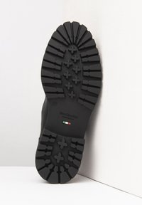 Suola in gomma nera con scanalature profonde e motivi a croce. Presenta un'etichetta con "Nero Giardini" e una bandiera italiana. È contrassegnata con la taglia 37.