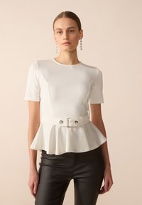 Hvit peplum topp med korte ermer, rund halslinning og to frontknapper; sammen med svarte tettsittende bukser. Glatt tekstur.
