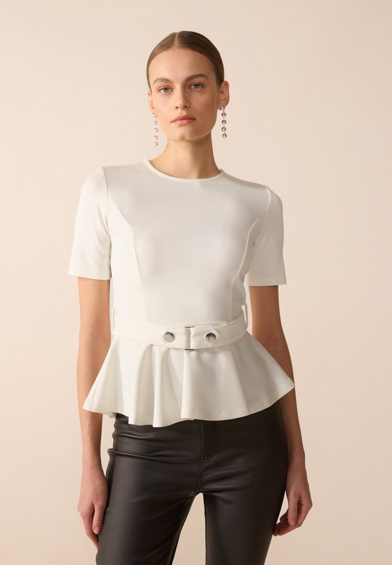 Valge peplum-top, lühikeste varrukatega, ümmarguse kaelusega ja kahe esiplaanil asuva nööbiga; koos mustade kitsaste pükstega. Sile tekstuur.