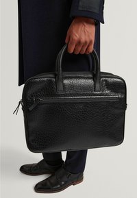 Schwarze Lederaktentasche mit strukturierter Oberfläche, zwei oberen Griffen und einer Reißverschlusstasche vorne. Verfügt über abgerundete Kanten und dezente Markenkennzeichnung.
