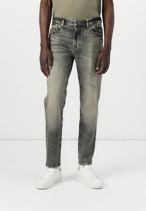 Jeans de denim gris claro con un diseño deslavado, presentan un desgaste sutil y una pernera entallada. Combinados con zapatillas blancas.