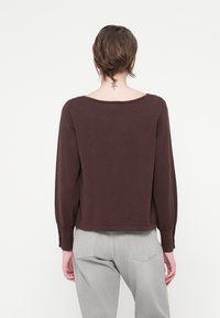 Brązowy sweter z dzianiny z długimi rękawami, szerokim dekoltem i prążkowanymi mankietami. Materiał wydaje się miękki i textured, z krojem cropped.