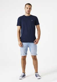 Camiseta de manga corta azul marino con un patrón texturizado de diamantes, combinada con pantalones cortos de mezclilla azul claro enrollados y zapatillas de deporte azul marino.