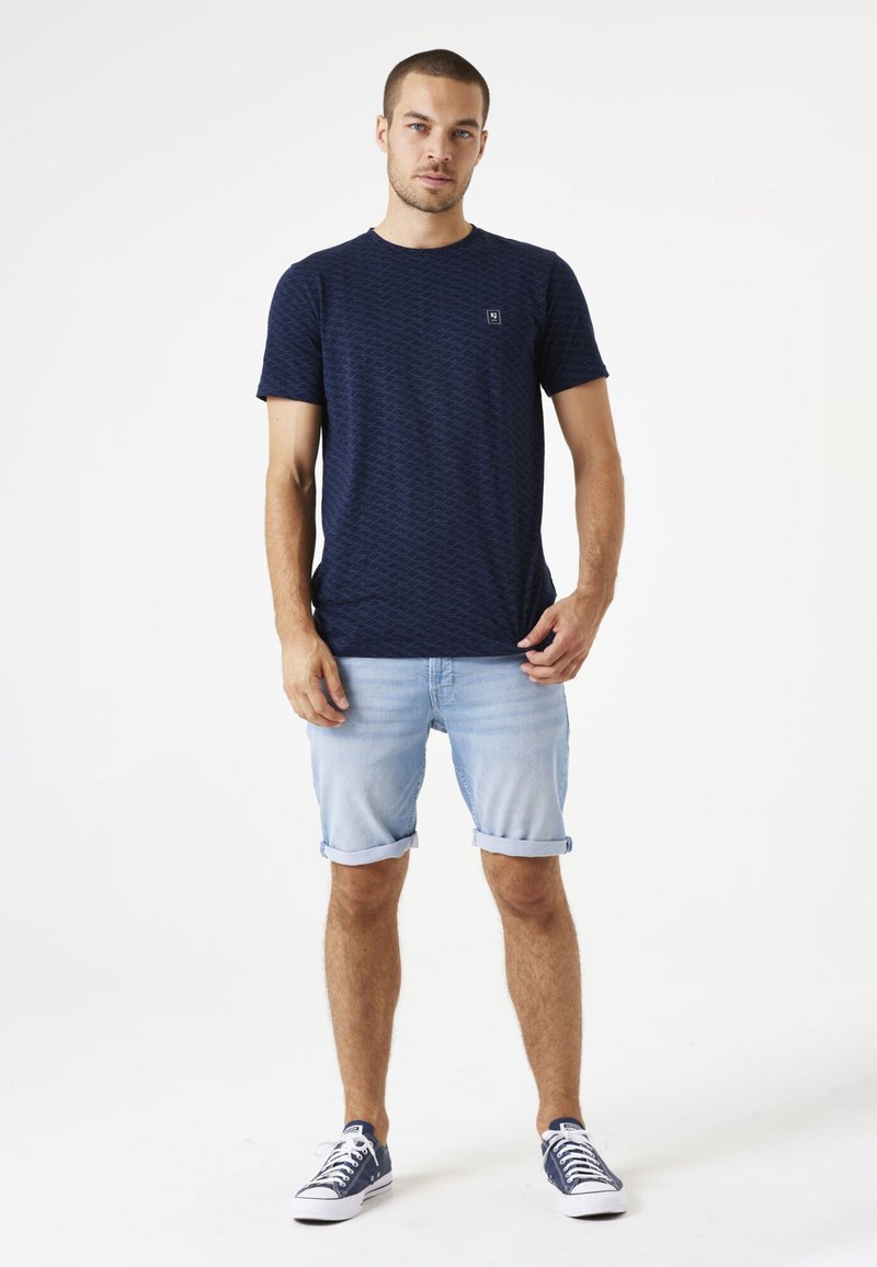 Camiseta de manga corta azul marino con un patrón texturizado de diamantes, combinada con pantalones cortos de mezclilla azul claro enrollados y zapatillas de deporte azul marino.