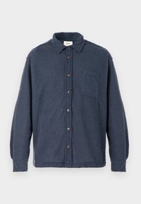 Μπλε σκούρο φλις πουκάμισο με υφή, κουμπιά στο μπροστινό μέρος, γιακά και τσέπη στο στήθος. Διαθέτει καφέ κουμπιά και μακριά μανίκια.