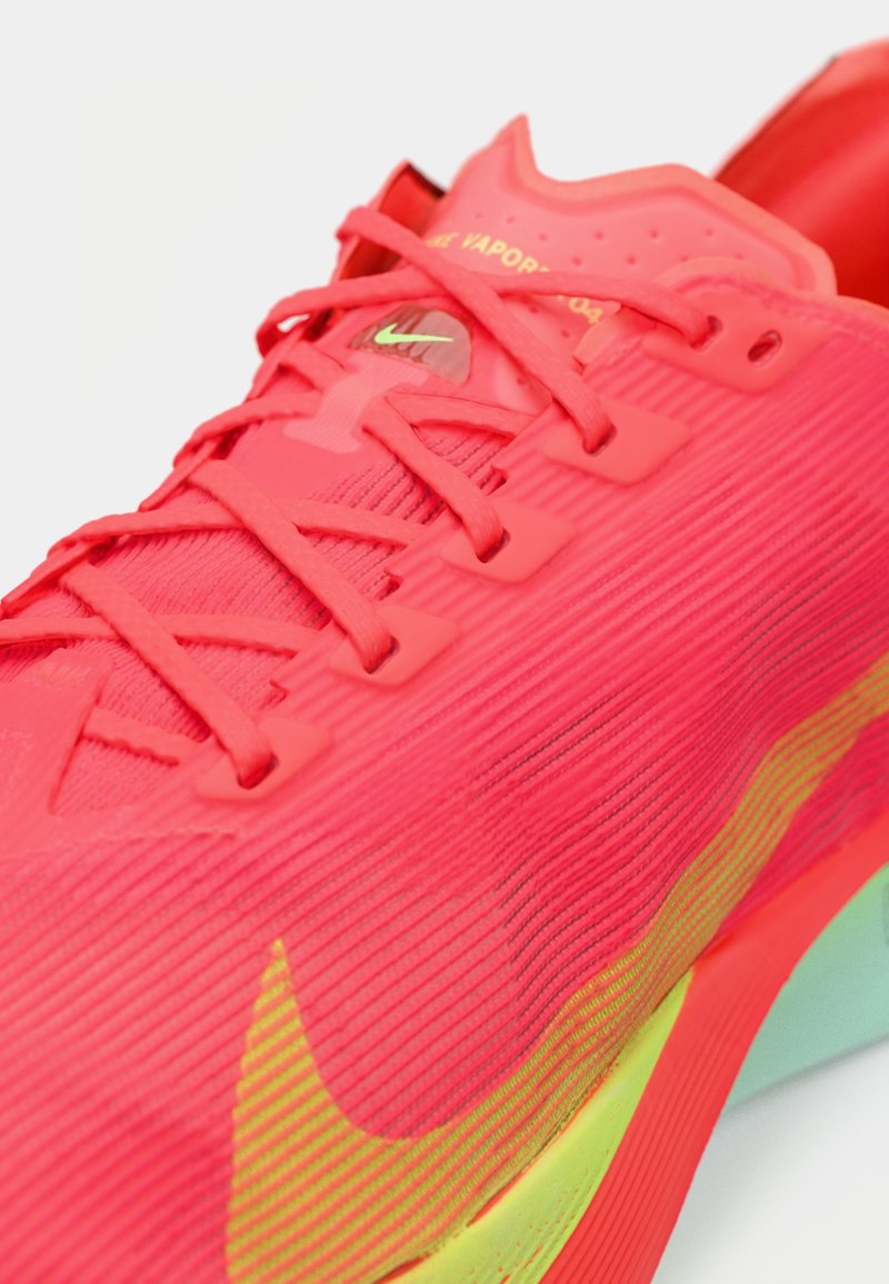 Zapatilla de running de Nike en un brillante color rosa, con un material texturizado, que cuenta con cordones estrechos, un acento verde en la suela y un diseño con patrón.