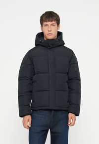 Sort pufferjakke med hætte, med et quiltet design og en frontlynlås. Inkluderer elastiske manchetter og to sidelommer.