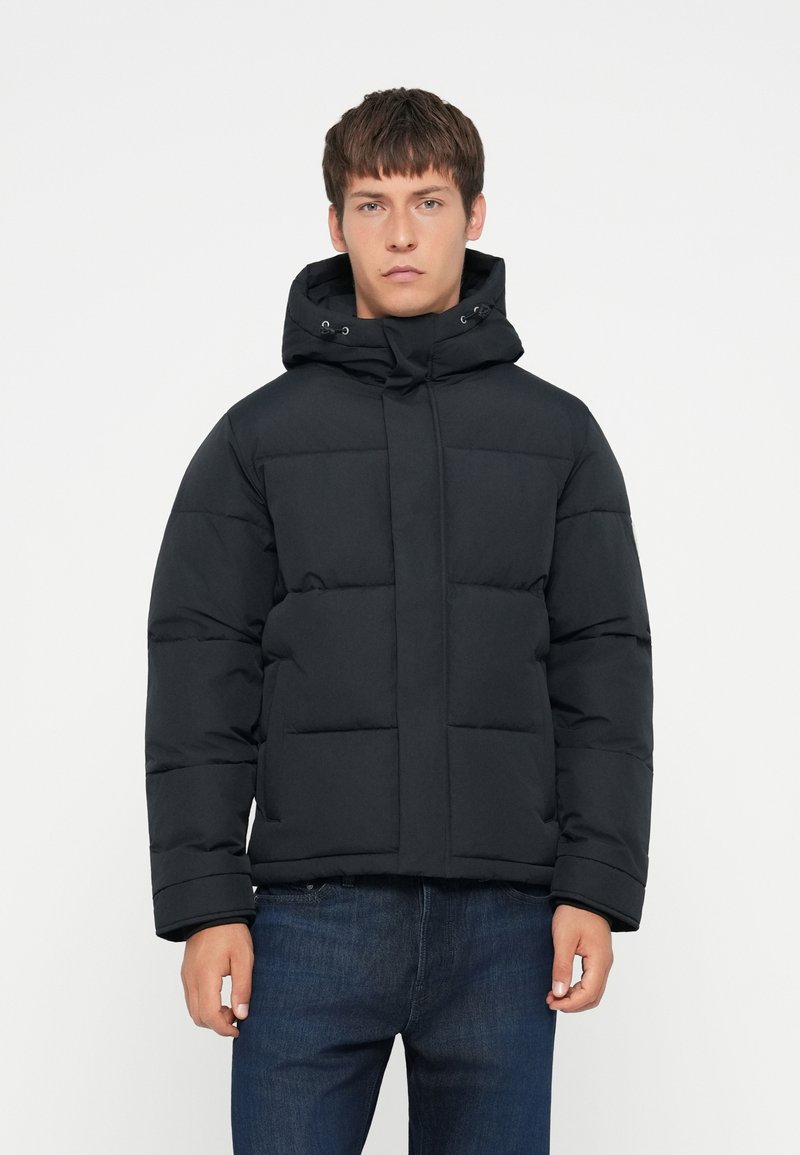 Sort pufferjakke med hætte, med et quiltet design og en frontlynlås. Inkluderer elastiske manchetter og to sidelommer.