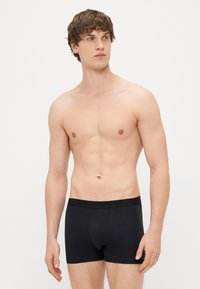 Črne bokserice iz gladkega, raztegljivega materiala z širokim elastičnim pasom. Prilegajoč dizajn in ojačan sprednji žep.