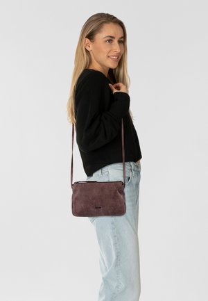 Borsa a tracolla compatta in materiale mauve texturizzato, con chiusura a zip e tracolla regolabile, abbinata a jeans azzurri chiari e a un maglione nero.