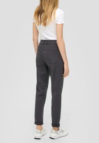 Pantalons gris taille haute avec une coupe décontractée, poignets retroussés, poches arrière, associés à un t-shirt blanc et des baskets claires.