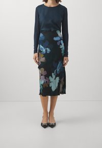 Tummansininen pitkähihaisen topin yhdistelmä, joka on yhdistetty tummapohjaiseen, kukkakuosisesti polvipituiseen hameeseen, jossa on sävyjä sinisestä, violetista ja vihreästä.