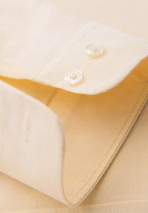 Lichtgele shirtkraag met twee witte knopen, netjes opgevouwen, met een soepele textuur en fijne stikseldetails.