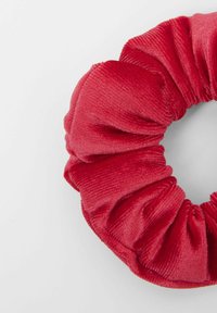 Červená sametová gumička s plyšovou texturou, kulatým tvarem a nařaseným designem, která poskytuje měkký a elegantní vzhled.