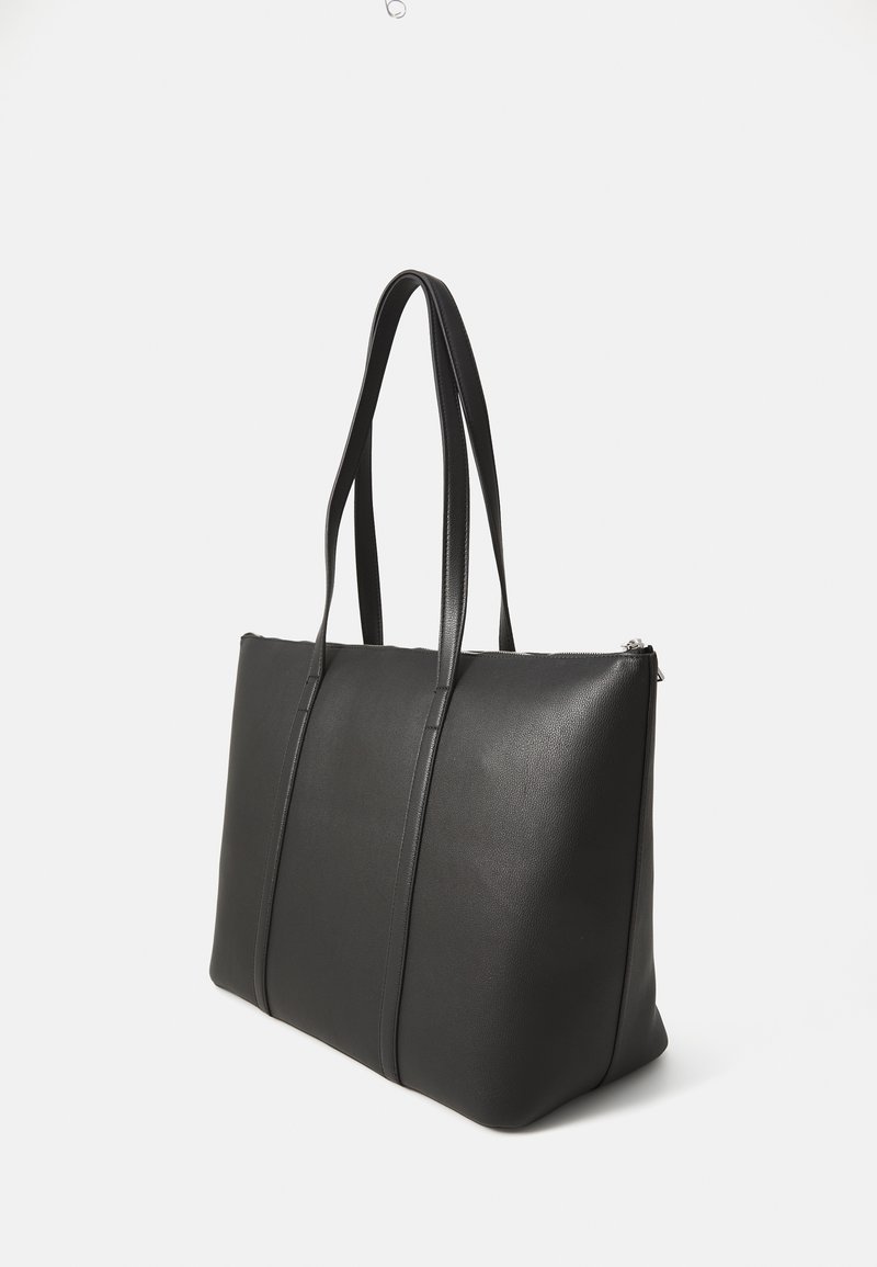 Sac fourre-tout en cuir noir avec deux longues poignées, texture lisse, forme rectangulaire et fermeture zippée en haut. Présente des détails de coutures verticales.