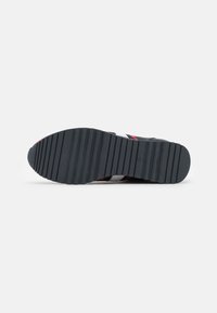 Suela de goma oscura con ranuras horizontales, con acentos rojos y blancos en una parte superior gris. Superficie plana y texturizada para agarre y tracción.