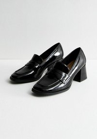 Black patent leather loafers with a square toe, a mid-height block heel, and a decorative strap across the vamp. Smooth, shiny texture.