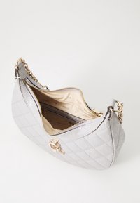 Lys grå quiltet håndtaske med guldkæde, guld lynlås og beige stofinteriør prydet med "GUESS" logoer.