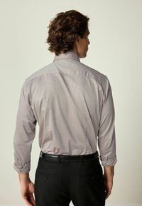 Cămașă cu mânecă lungă în violet deschis, cu un model geometric subtil, asortată cu pantaloni negri și o curea neagră, evidențiind un design ajustat.