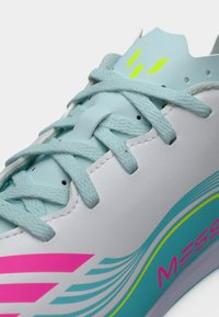 Αθλητικό παπούτσι με κορδόνια, με λείο λευκό πάνω μέρος, μπλε έμφαση, ροζ γραμμές και πράσινο λογότυπο, με υφή στην επιφάνεια και επενδυμένη γλώσσα.