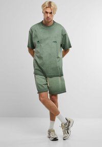 Zelené bavlnené tričko s oversize strihom a krátkymi rukávmi, v kombinácii s rovnakými zelenými šortkami s elastickým pásom a šnúrkou.