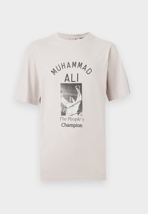 Beige Baumwoll-T-Shirt mit einem zentralen Grafik von Muhammad Ali, der Text darüber lautet "MUHAMMAD ALI" und darunter "Der Champion des Volkes."