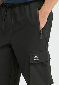 Svarte cargo-shorts med elastisk midje, sidelommer med glidelås og en lommelukking med borrelås som har "North Bend"-logo. Glatt, lett materiale.