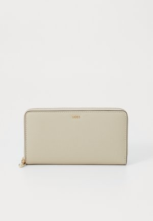 Long beige wallet made of smooth leather with a zip closure, features a small metallic accent, and embossed brand logo on the front.