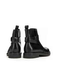 Černé kožené kotníkové boty s hladkým povrchem, které mají široký pásek a detailem na přezku, robustní podrážky a poutka na zadní straně.