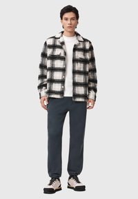 Czarna i biała koszula w kratę z flaneli, biała koszulka typu crew neck, ciemne dresy i jasne sneakersy z czarną podeszwą i sznurówkami.