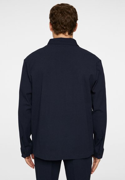 Donkerblauwe langemouwenshirt met een kraag, knoopmanchetten en een gladde textuur; heeft een rechte zoom en een ontspannen pasvorm.