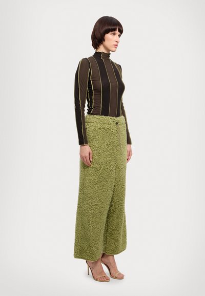 Pantalons larges en polaire verte avec une surface texturée, associés à un haut ajusté à manches longues noir et jaune avec des rayures. Sandales à talons simples avec des lanières.