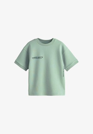 T-shirt en coton vert menthe à manches courtes, avec des graphismes en texte noir à l'avant et sur le côté. Encolure ronde et coupe décontractée.