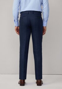 Pantaloni tailored blu navy con una trama liscia, passanti per cintura e due tasche posteriori. Abbinati a scarpe in pelle marrone e una camicia azzurra chiara.
