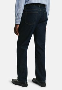 Jeans de mezclilla azul oscuro con corte recto, que cuentan con dos bolsillos traseros y un cinturón trenzado negro texturizado, usados con zapatos negros.