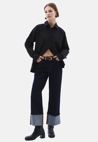 Zwarte button-up overhemd, donkere denim broek met opgevouwen lichtblauwe manchetten, en zware zwarte enkellaarsjes. Bevat een bordeauxrode riem met een zilveren gesp.