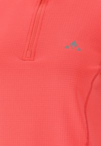 Leichter Pullover aus Korallenstoff mit einem halben Reißverschluss, strukturierter Oberfläche und einem kleinen grauen Logo auf der oberen linken Seite.