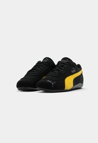 Sneaker in suede nero e giallo con dettagli texturizzati, punta arrotondata, chiusura con lacci e suola in gomma. Presenta accenti del logo Puma.